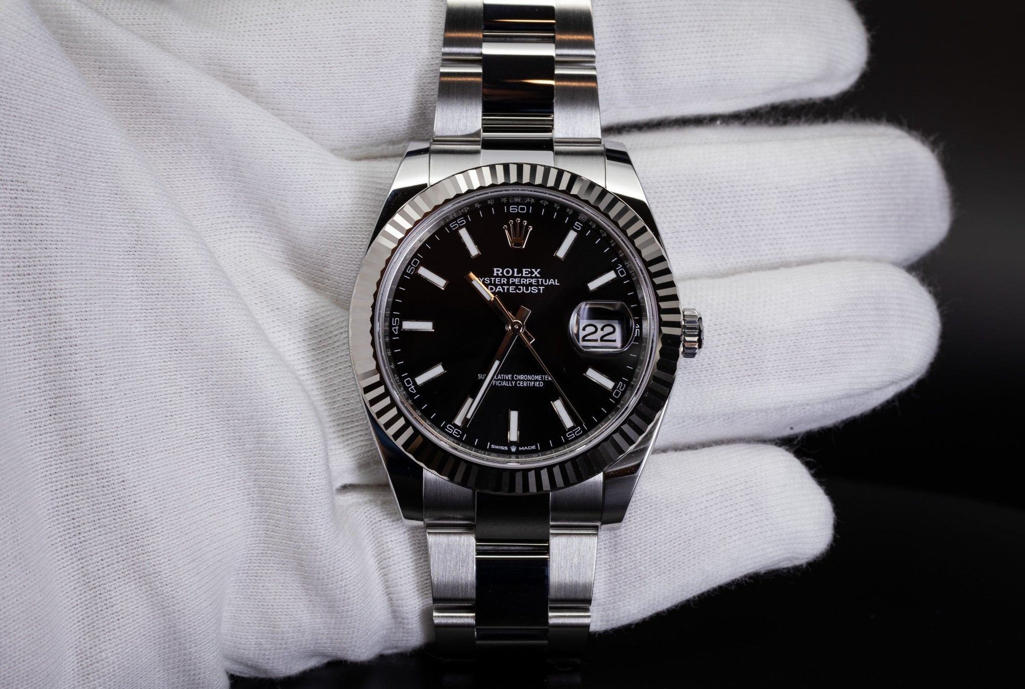 Rolex Datejust with black dial and stainless steel bracelet held in a white glove during inspection