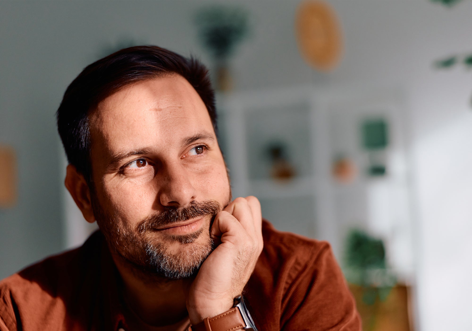 Man in a brown shirt with a thoughtful expression, indoors with a blurred background